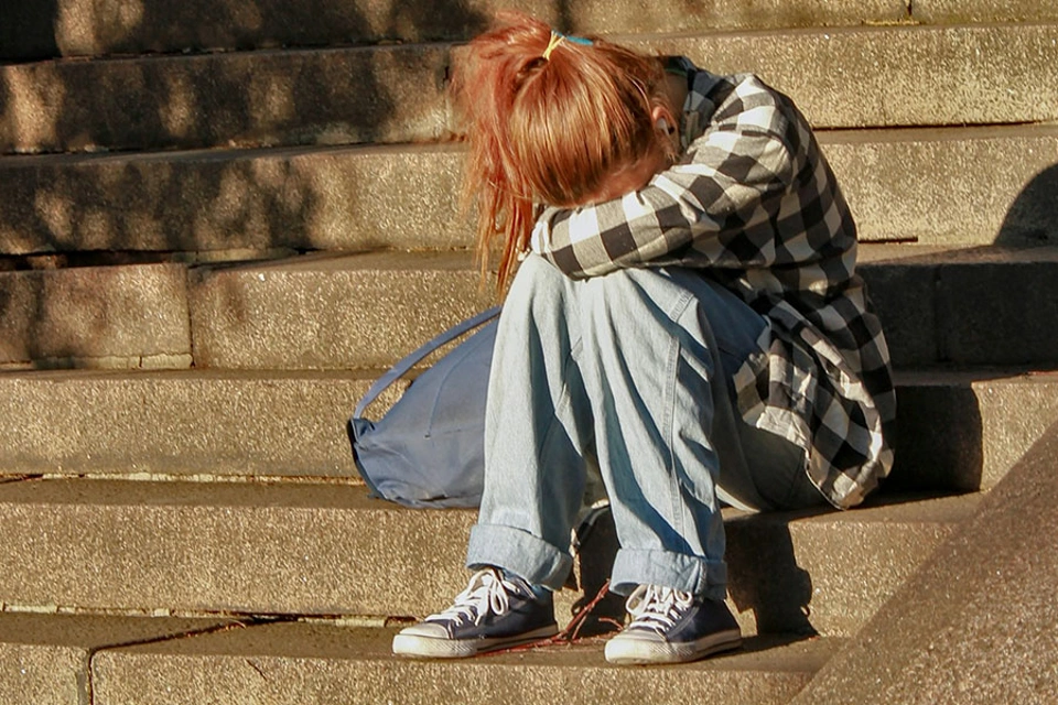 Mädchen sitzt mit dem Kopf in den verschränkten Armen auf einer Treppe Mädchen sitzt mit dem Kopf in den verschränkten Armen auf einer Treppe